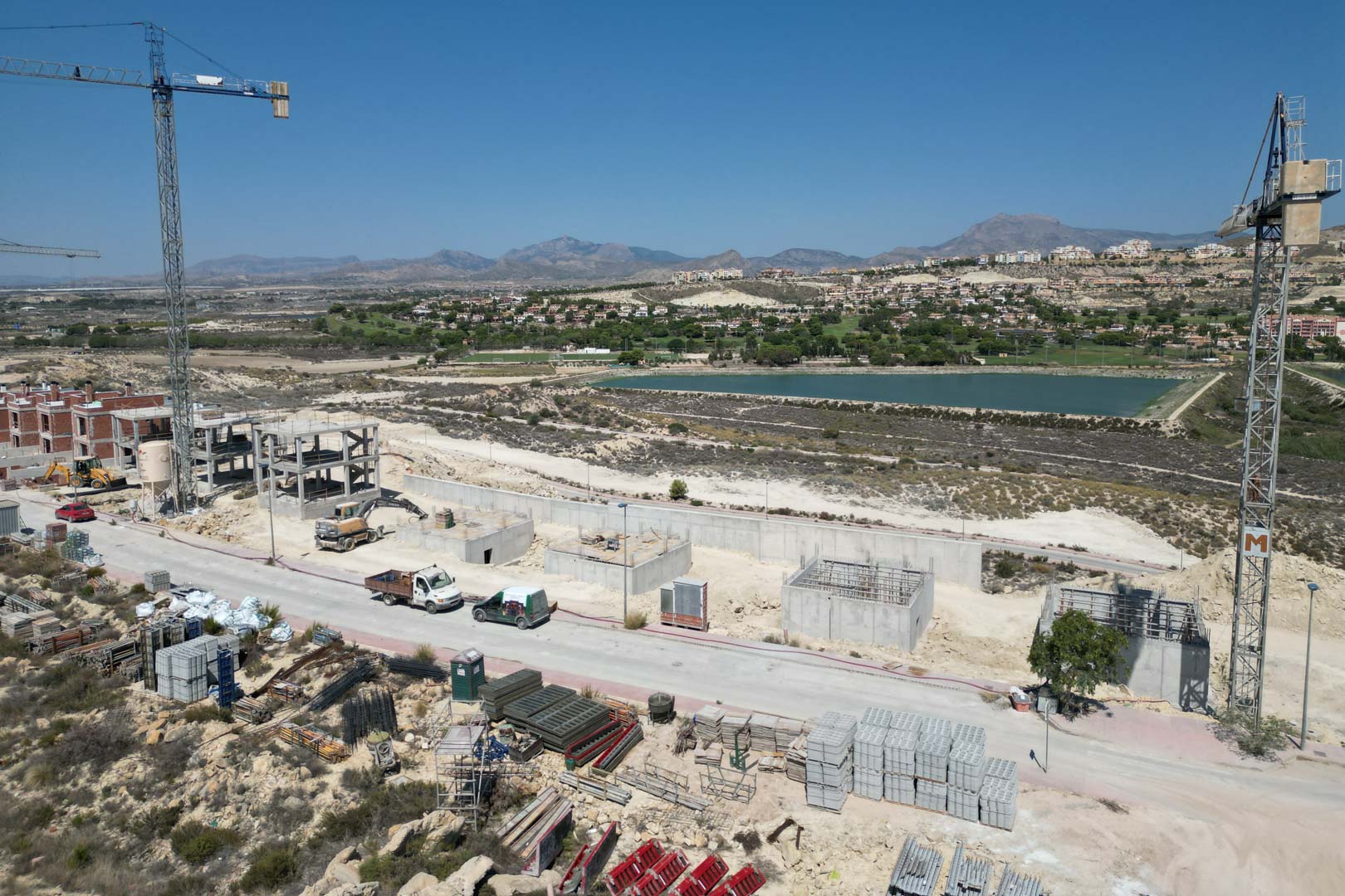 Vista aérea de la fase de construcción de las villas, mostrando las estructuras de hormigón, grúas y el entorno natural con vistas al lago y las montañas.