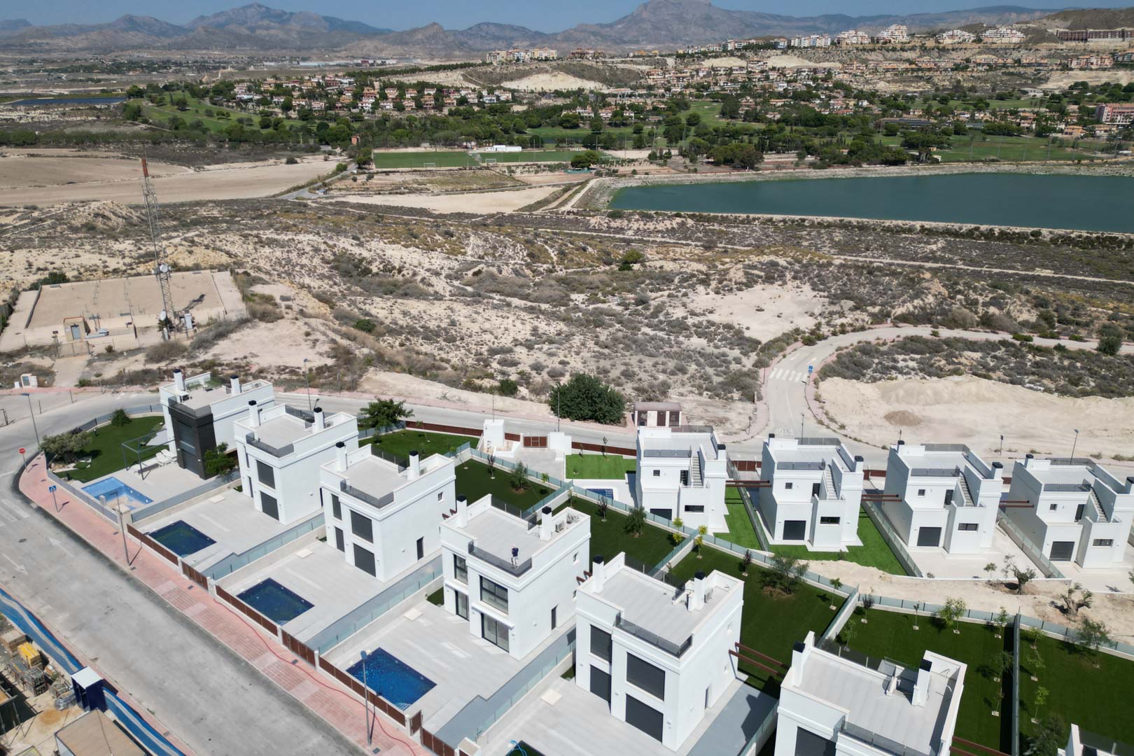Vista aérea de villas contemporáneas con piscinas privadas y jardines, situadas junto a un campo de golf y un embalse con vistas a la montaña.