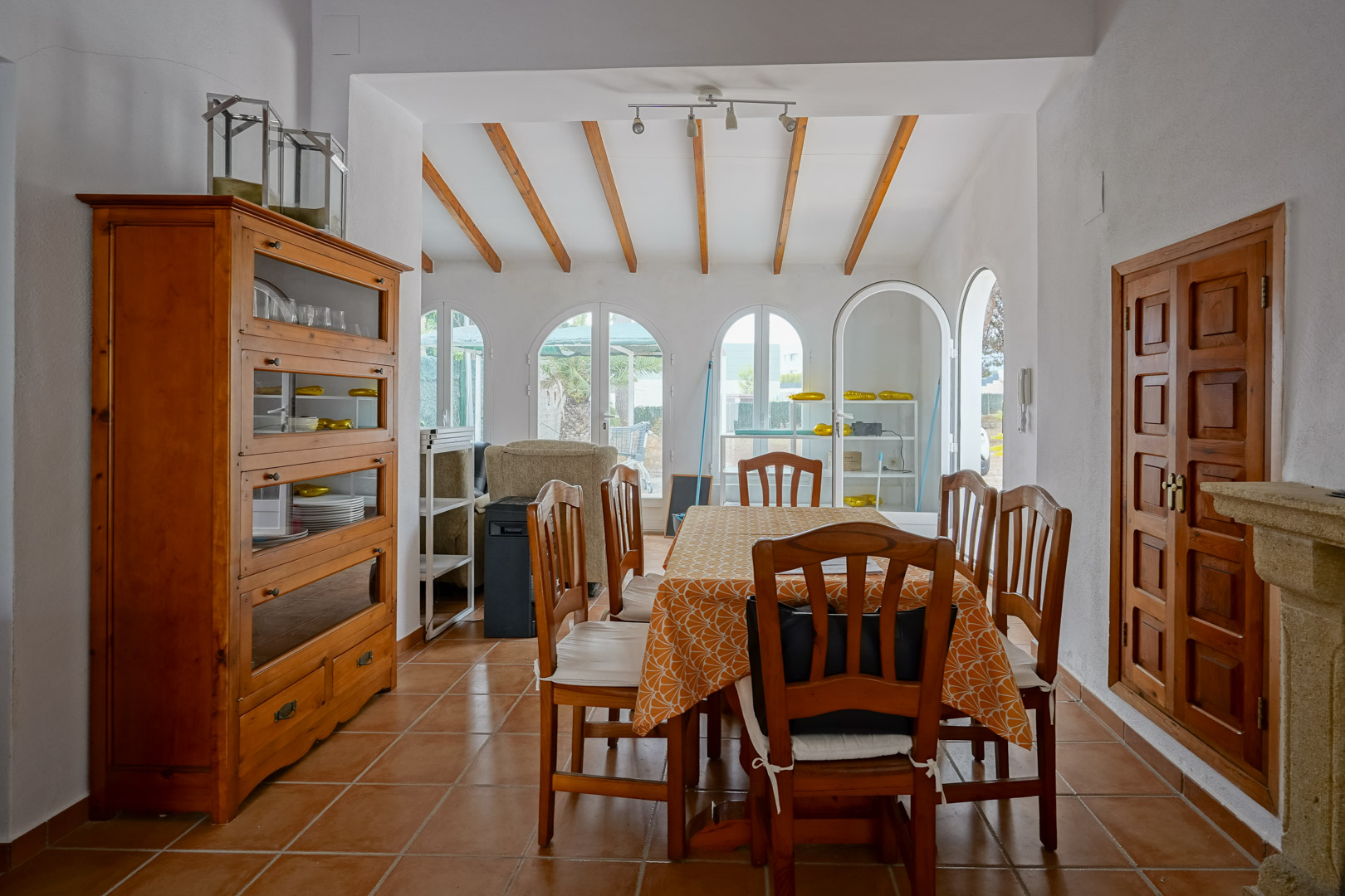 Comedor con vigas de madera a la vista, suelos de terracota y amplios ventanales de arco que aportan luz natural y acceso al exterior.