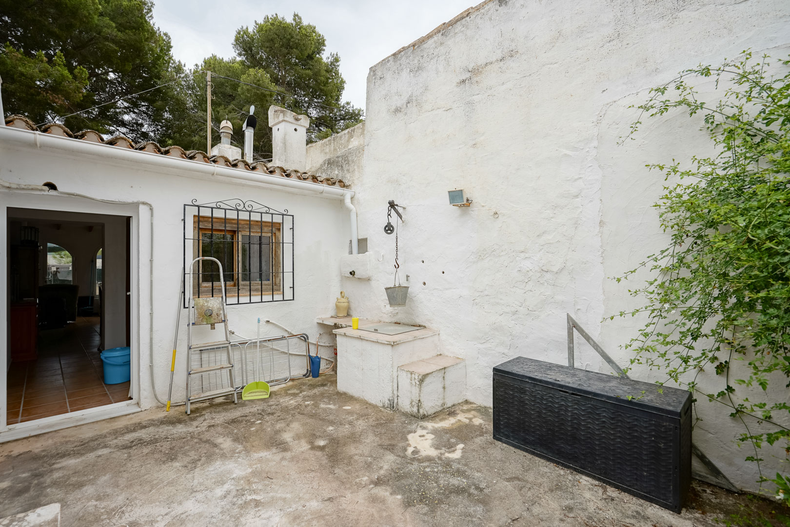 Patio exterior con pozo tradicional y polea, muros encalados y acceso directo a la vivienda bajo una cubierta de teja cerámica.