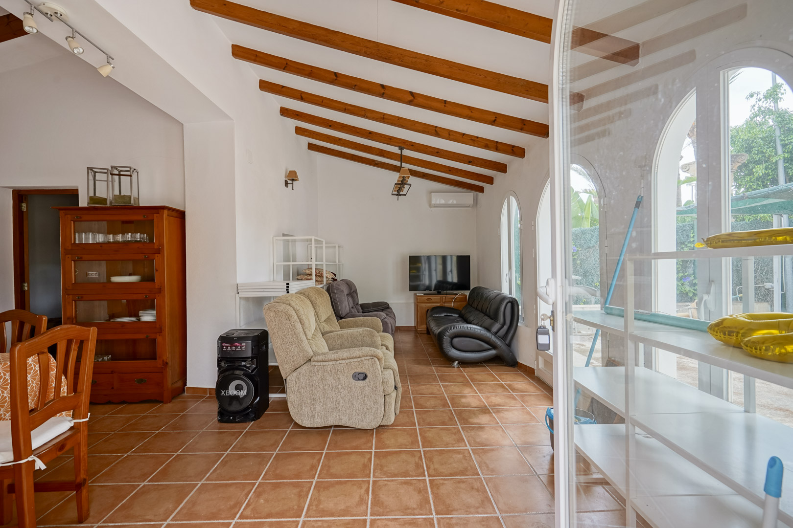 Salón con techos altos de vigas de madera vista, suelos de terracota y ventanales de arco que aportan luz natural y acceso al exterior.
