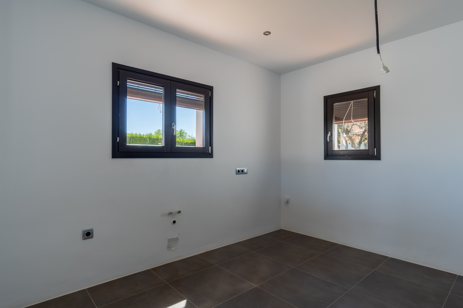 Zona preparada para la instalación de cocina con suelos cerámicos oscuros, ventanas de aluminio con acabado madera y preinstalaciones de fontanería y electricidad.