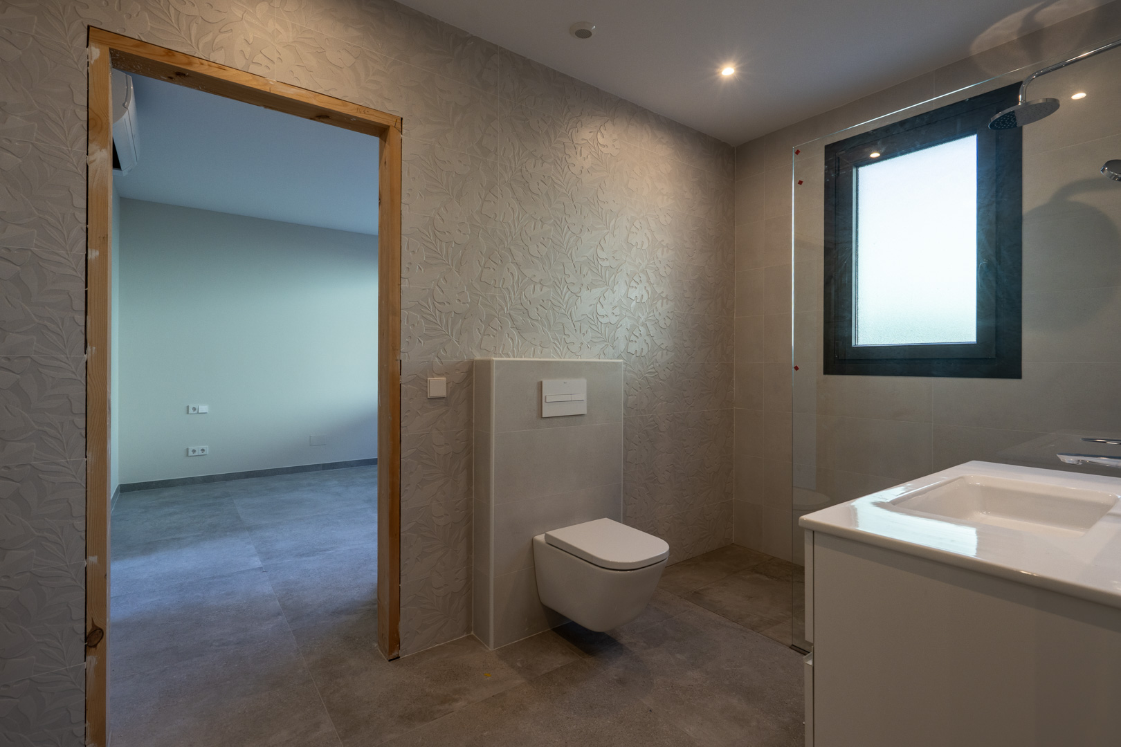 Detalle de baño moderno con paredes texturizadas y ducha con mampara.