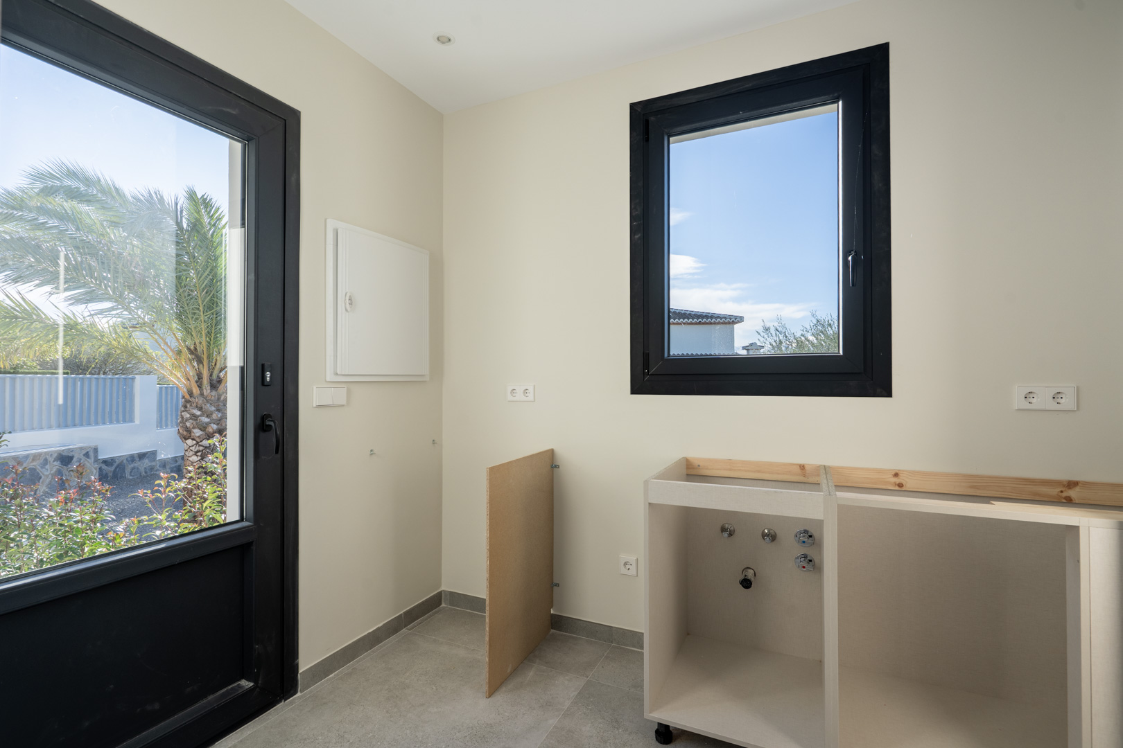 Detalle del lavadero con puerta al jardín, ventana con marco negro y mueble bajo en obra.