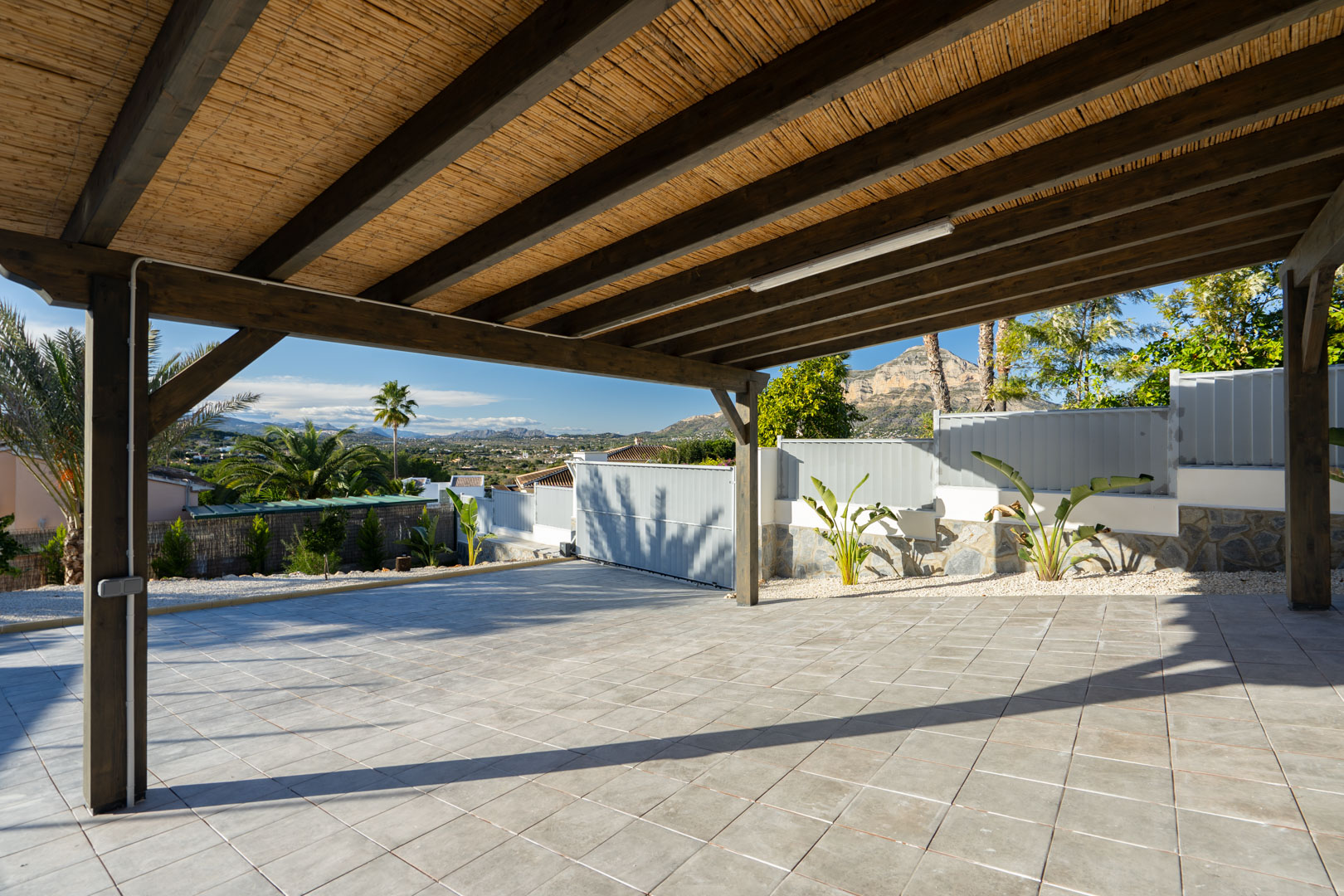 Pérgola con techo de caña y suelo embaldosado, con vistas a la vegetación y montañas.