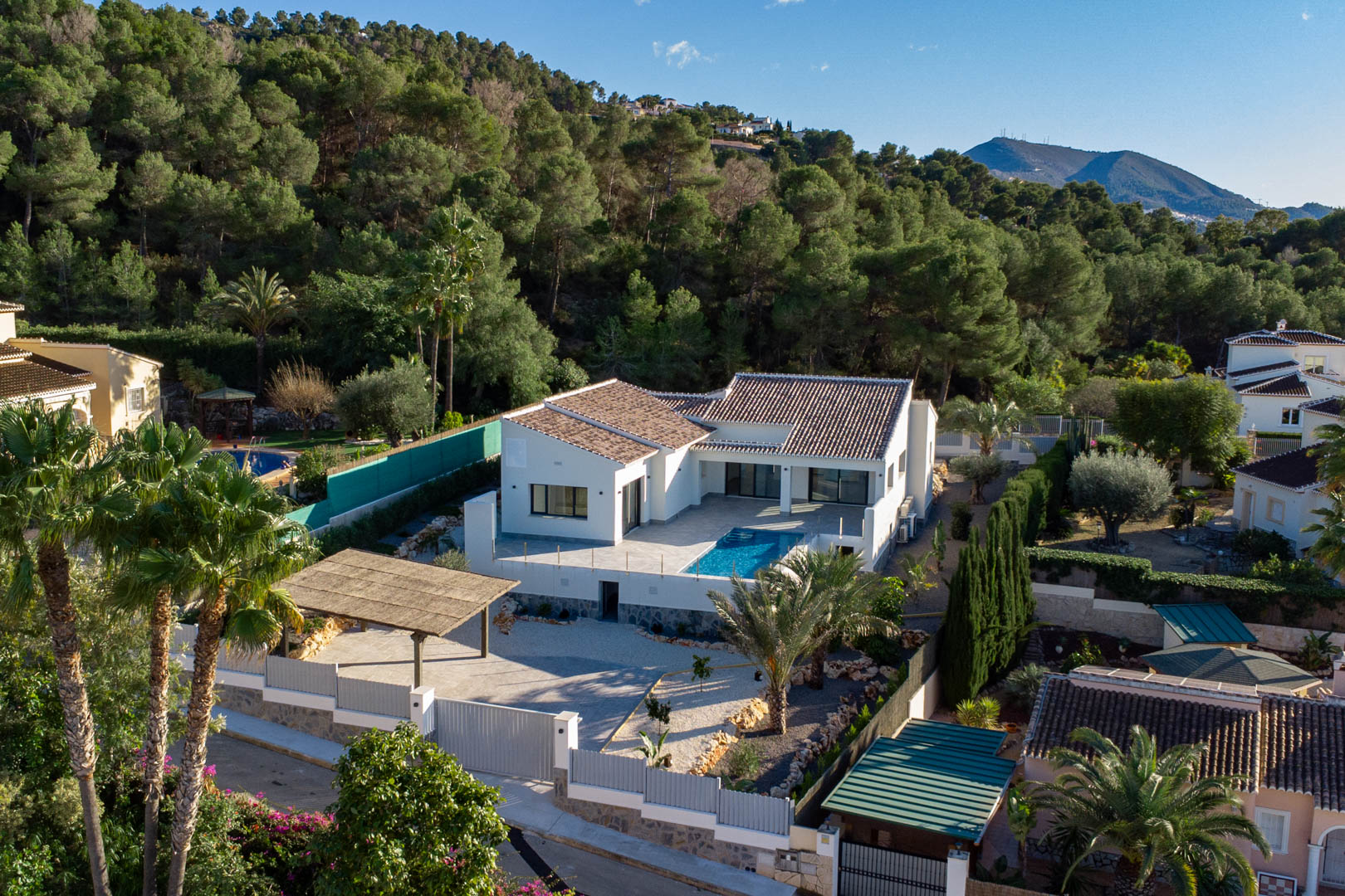 Vista aérea de villa moderna con piscina, rodeada de vegetación exuberante y aparcamiento cubierto en Jávea.