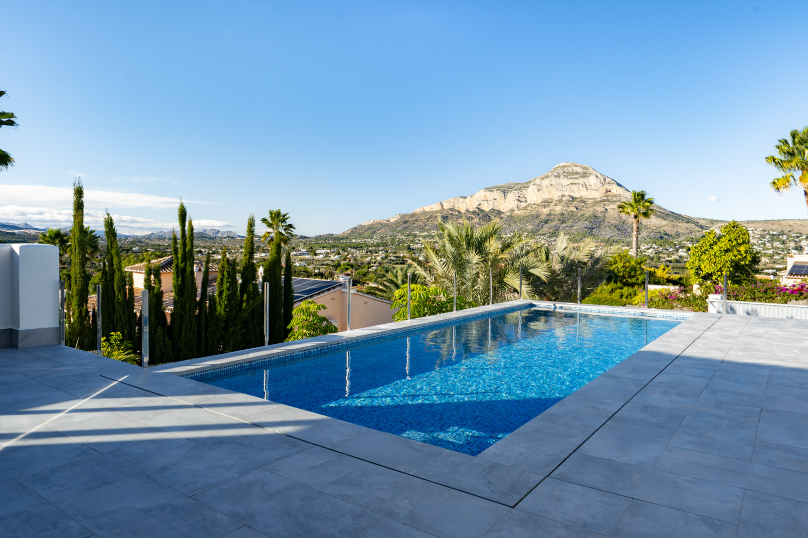 Vista de la piscina privada con azulejos azules y borde gris, con vistas panorámicas a la montaña y al paisaje.