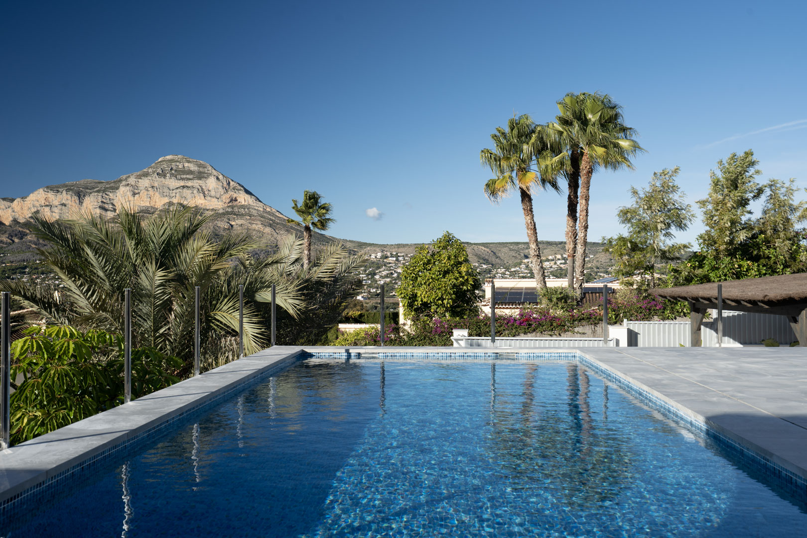 Vista de la piscina privada con mosaicos azules, rodeada de vegetación y con una montaña imponente al fondo.