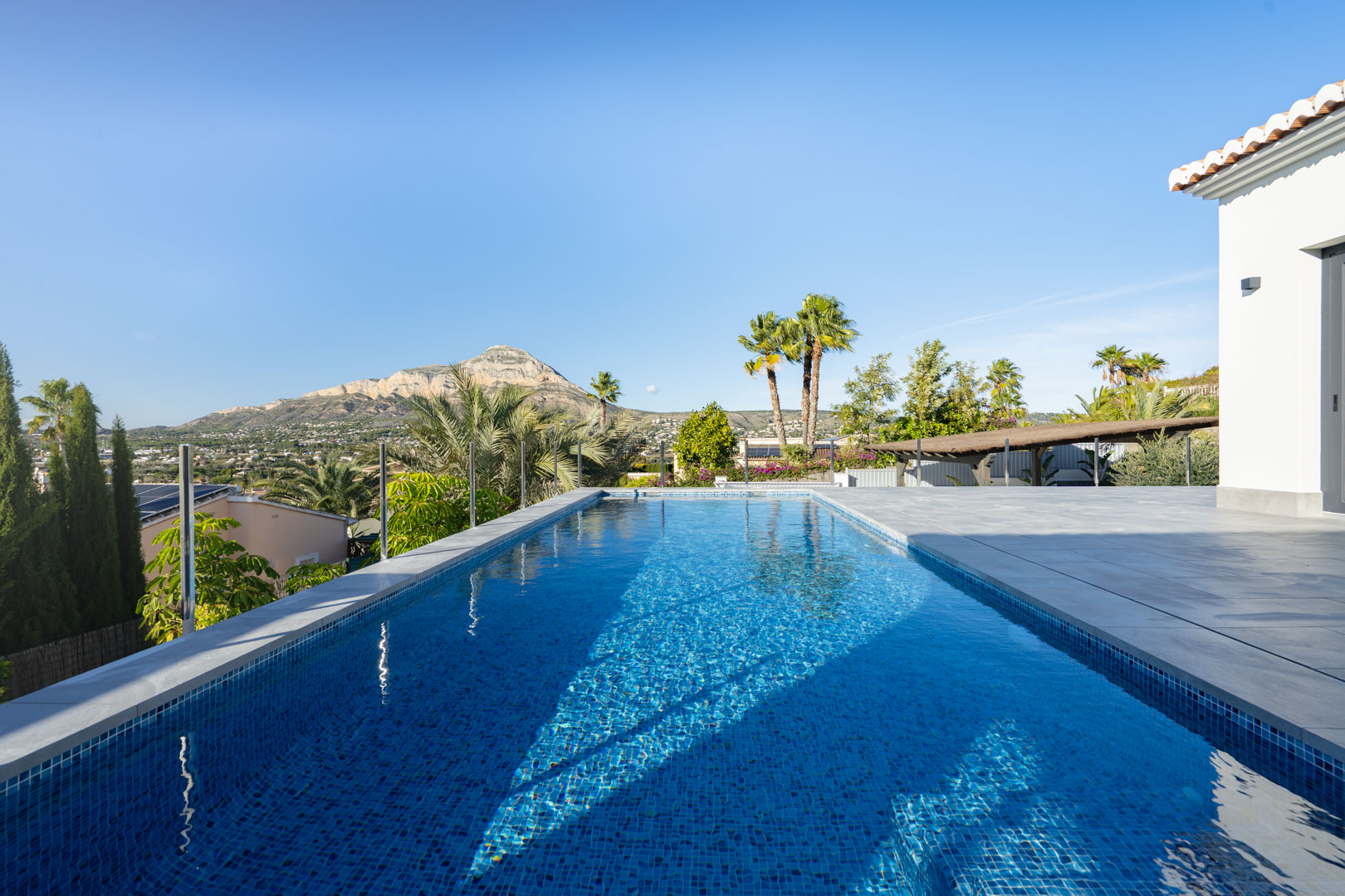 Vista de la piscina privada con mosaicos azules, terraza de baldosas grises y vistas a la montaña en Jávea.