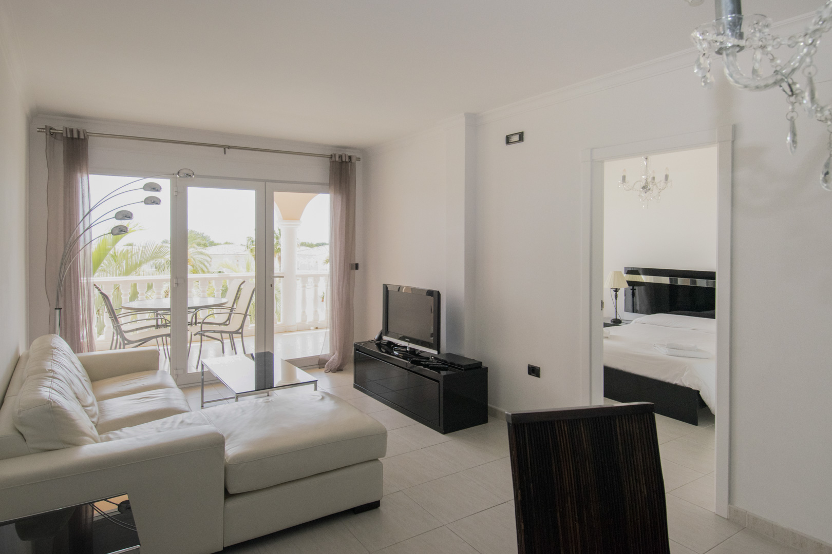 Salón con sofá de cuero blanco, muebles negros y acceso a la terraza. La estancia integra iluminación de diseño y ofrece una vista directa al dormitorio principal.