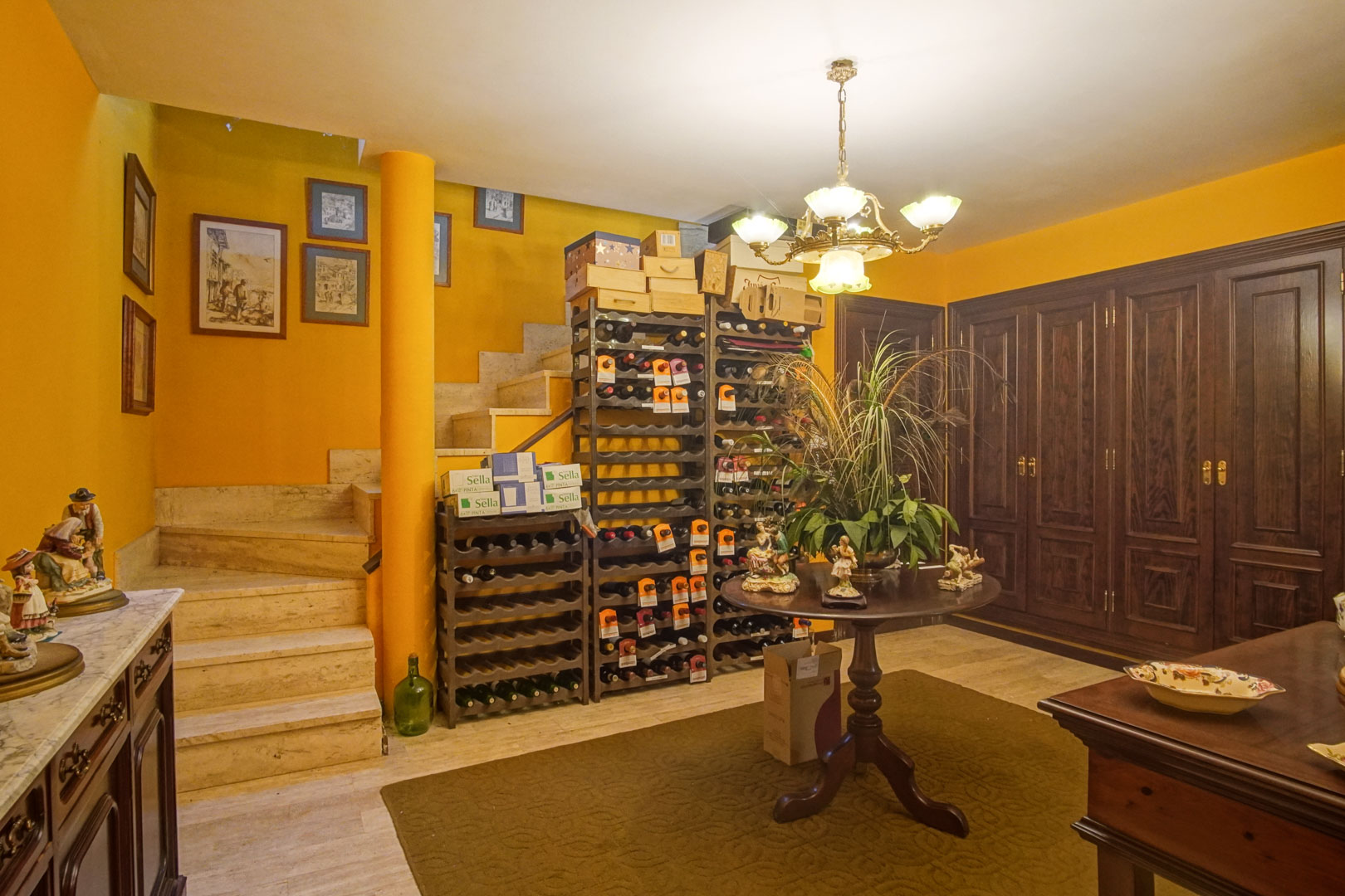 Bodega en planta inferior con estanterías para vino, suelos de mármol y amplios armarios empotrados de madera oscura junto a la escalera.