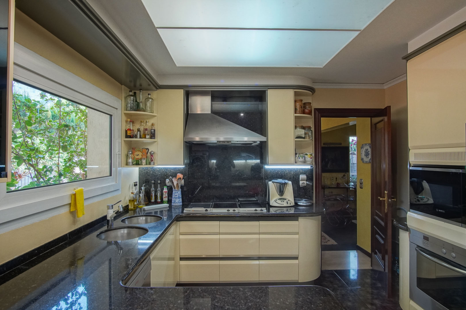 Cocina independiente equipada con encimera de granito oscuro, mobiliario en tono crema y electrodomésticos integrados bajo un amplio panel de iluminación cenital.