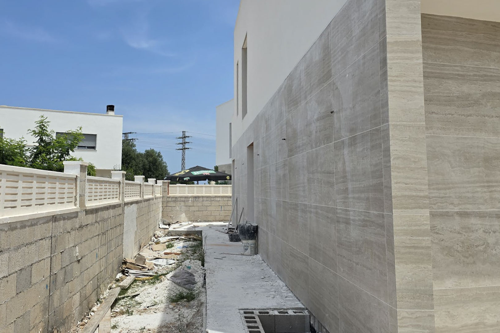 Fachada lateral en construcción revestida con piezas de gran formato en tono crema, mostrando la evolución de los acabados exteriores y el muro perimetral.