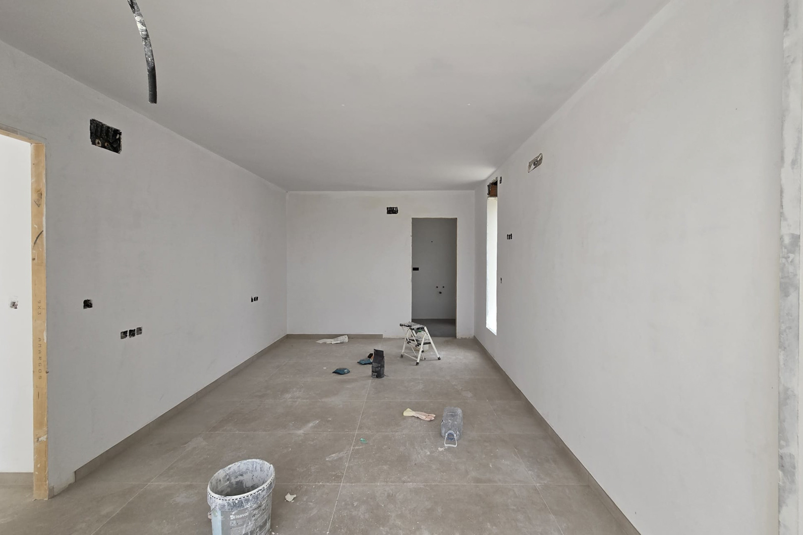 Interior en fase de acabado con suelo de gres porcelánico de gran formato y paredes blancas. Se observan las preinstalaciones eléctricas y accesos a estancias contiguas.
