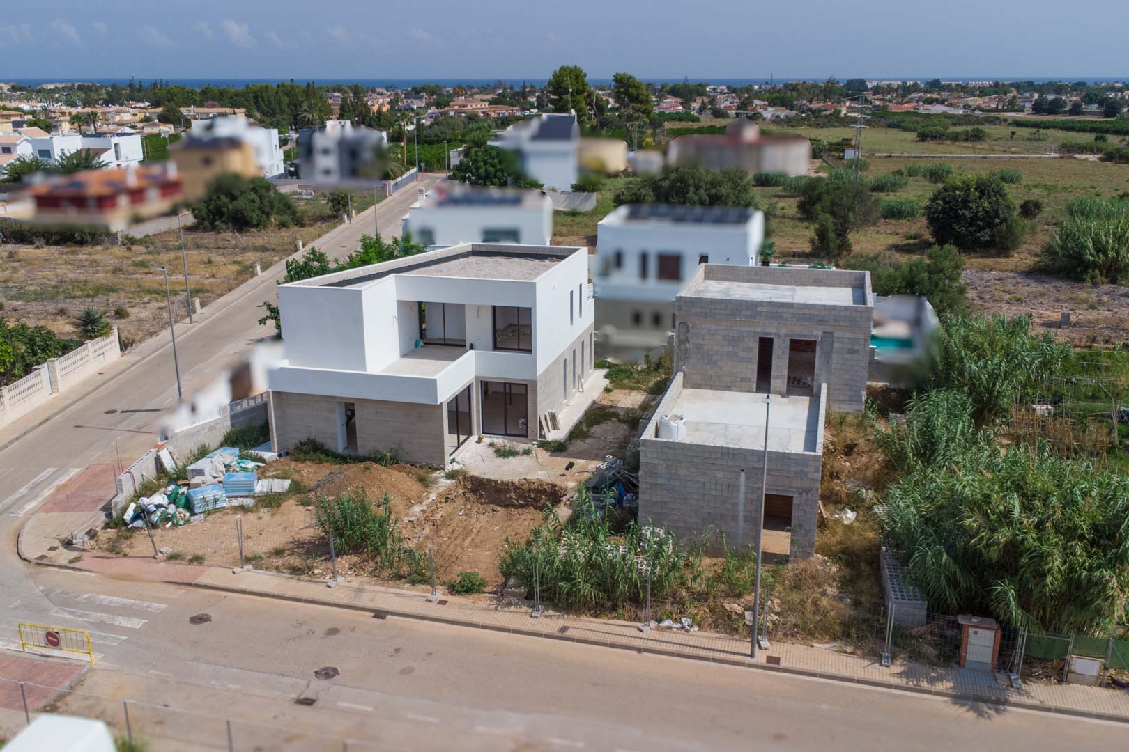 Vista aérea del proyecto residencial en El Vergel, mostrando dos villas modernas en fase de construcción con fachadas blancas y vistas despejadas hacia la costa mediterránea.