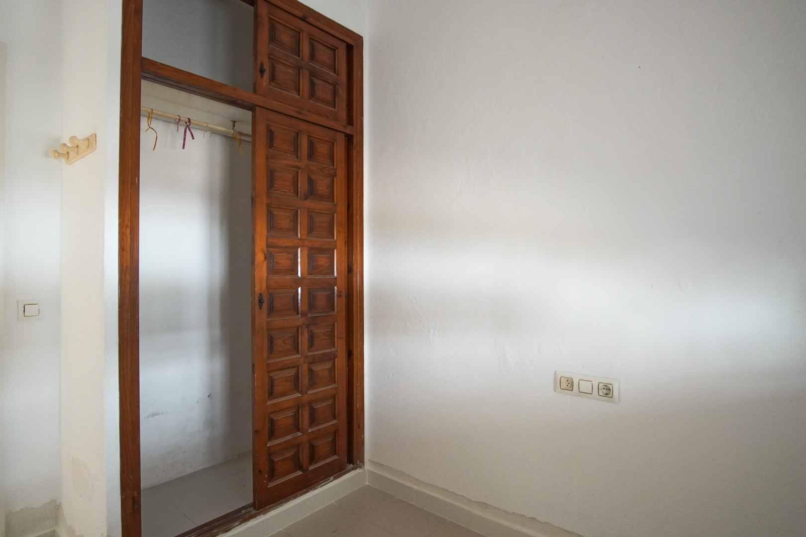 Dormitorio con armario empotrado de madera oscura y puertas correderas de diseño panelado. Las paredes blancas texturizadas contrastan con la carpintería clásica.