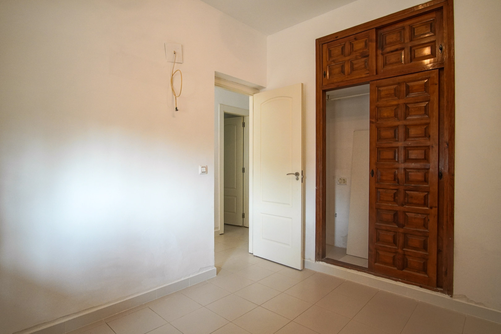 Dormitorio con armario empotrado de madera tallada y suelos cerámicos. La estancia conecta con el pasillo y ofrece potencial para personalización mediante reforma.