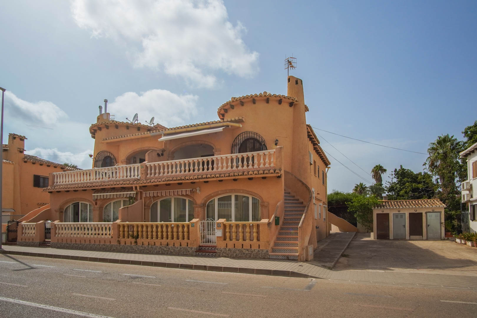 Fachada exterior de estilo mediterráneo con arcos, barandillas de piedra y escalera lateral decorada con azulejos, situada a pie de calle en Dénia.