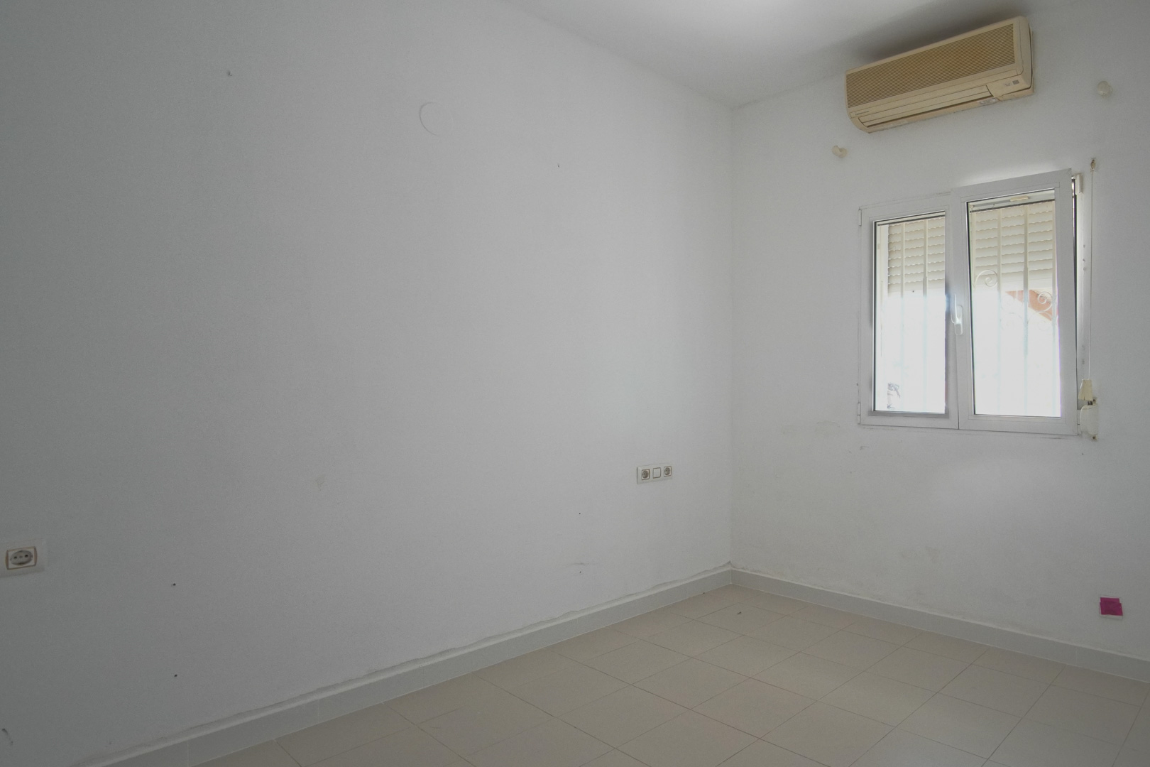 Habitación luminosa con paredes blancas, suelos de gres y unidad de aire acondicionado. Dispone de ventana de PVC con persiana integrada y tomas eléctricas.