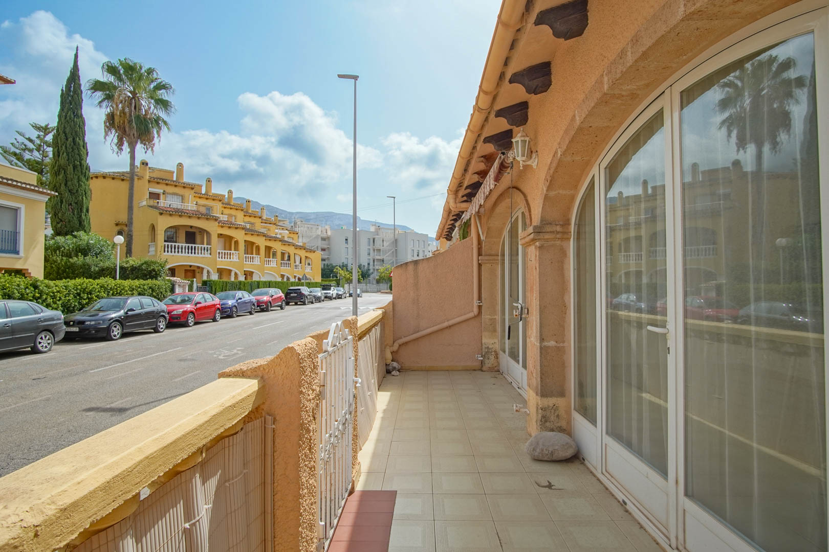 Terraza exterior con suelo cerámico y grandes ventanales de arco que dan acceso a la vivienda, situada frente a una tranquila calle residencial en Dénia.