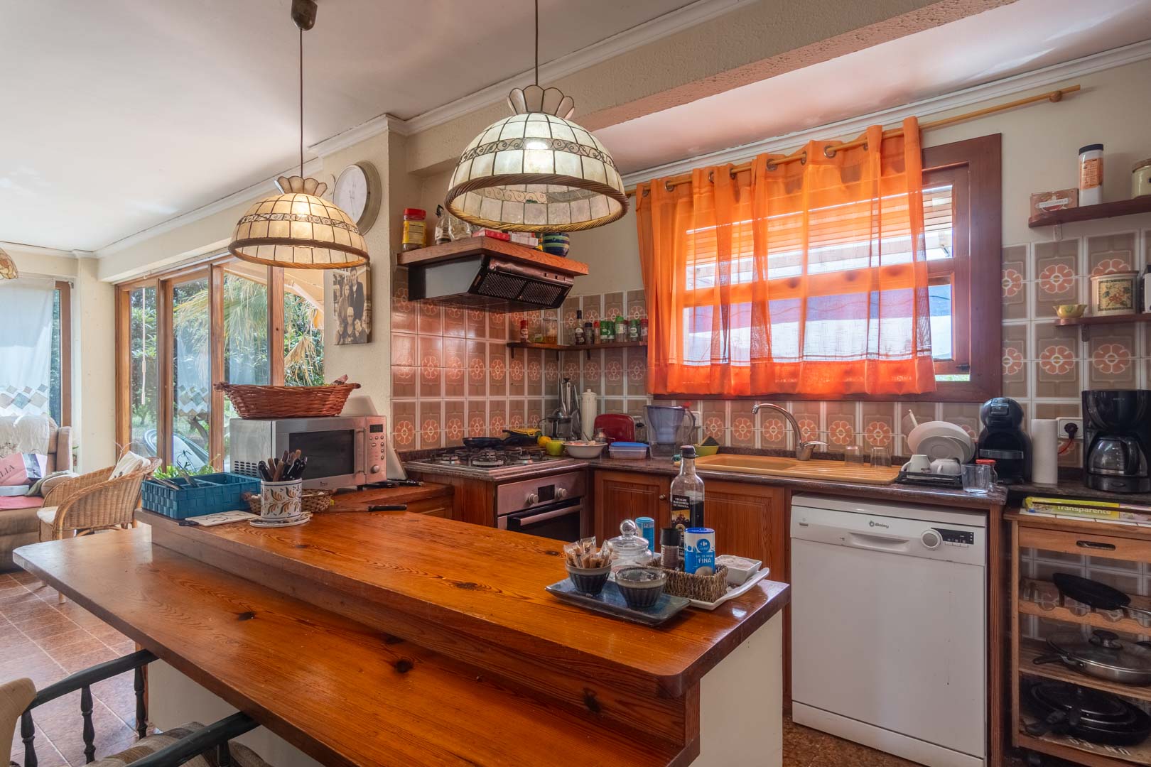 Cocina de estilo rústico con barra de madera maciza, azulejos tradicionales con motivos florales y lámparas colgantes decorativas junto a la zona de estar.