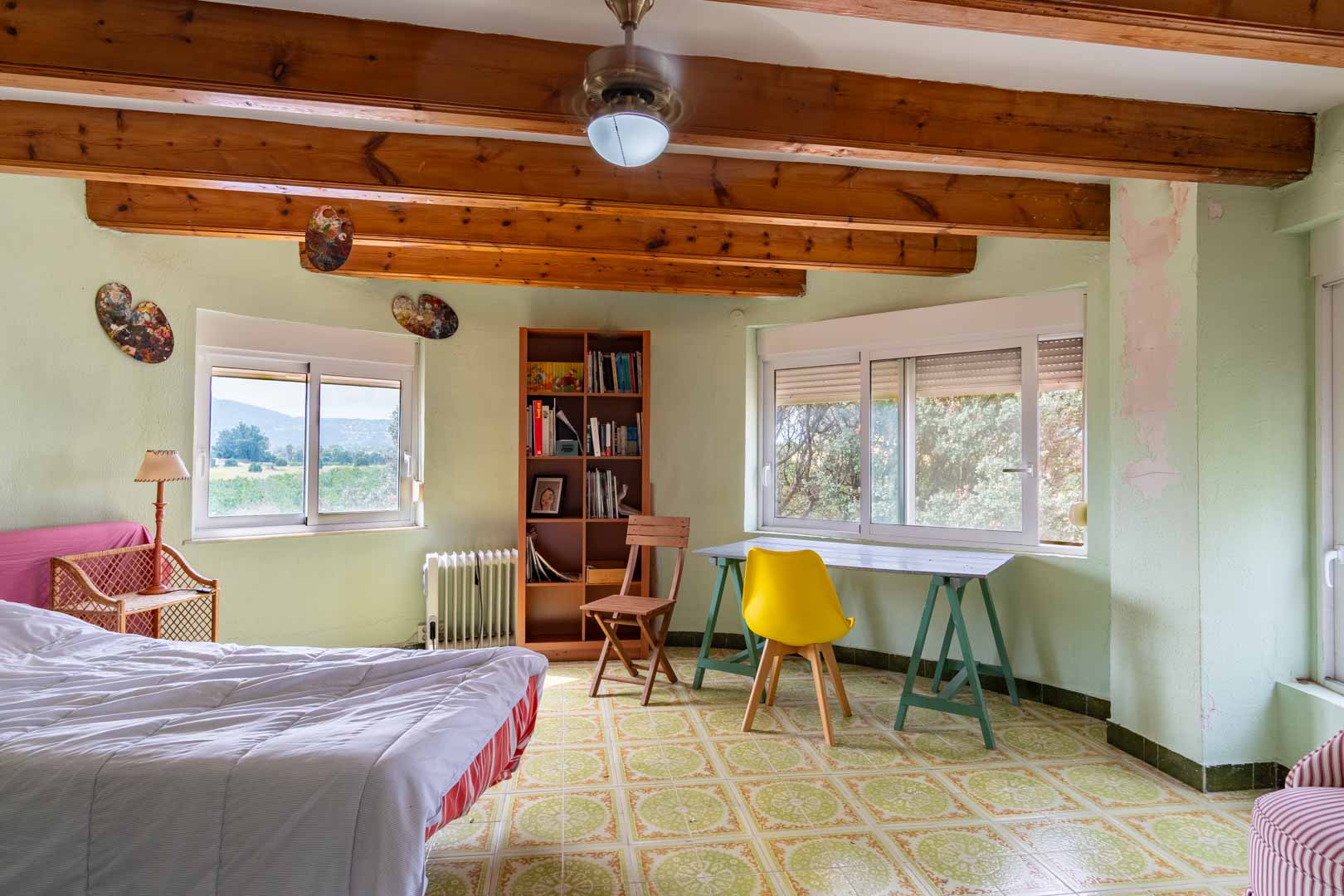 Dormitorio luminoso con vigas de madera a la vista, suelos de cerámica decorada y zona de estudio. Dispone de amplios ventanales con vistas despejadas al entorno natural.