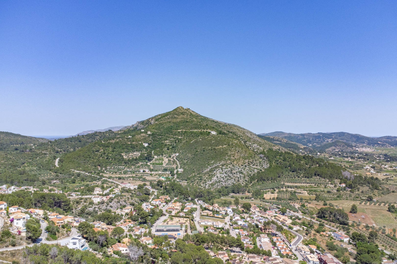Vista aérea panorámica del valle de Jalón en Alcalalí, destacando el entorno montañoso y la integración del núcleo residencial con el paisaje natural mediterráneo.