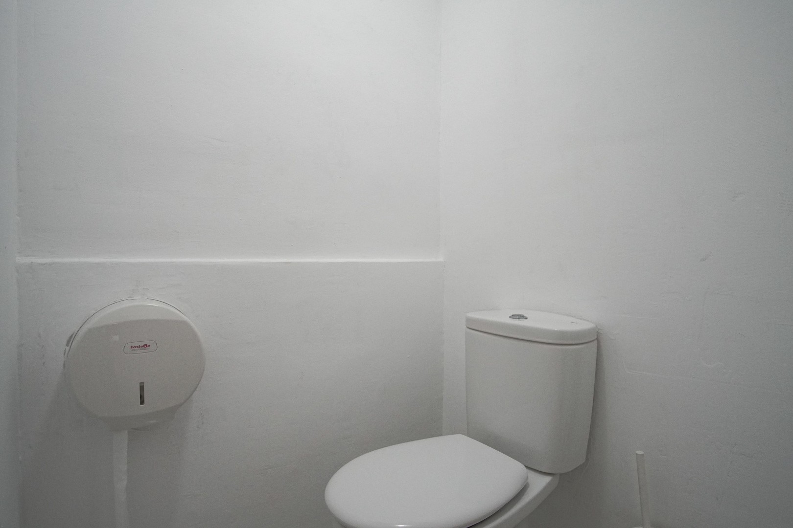 Detalle de un aseo con paredes blancas y dispensador de papel.