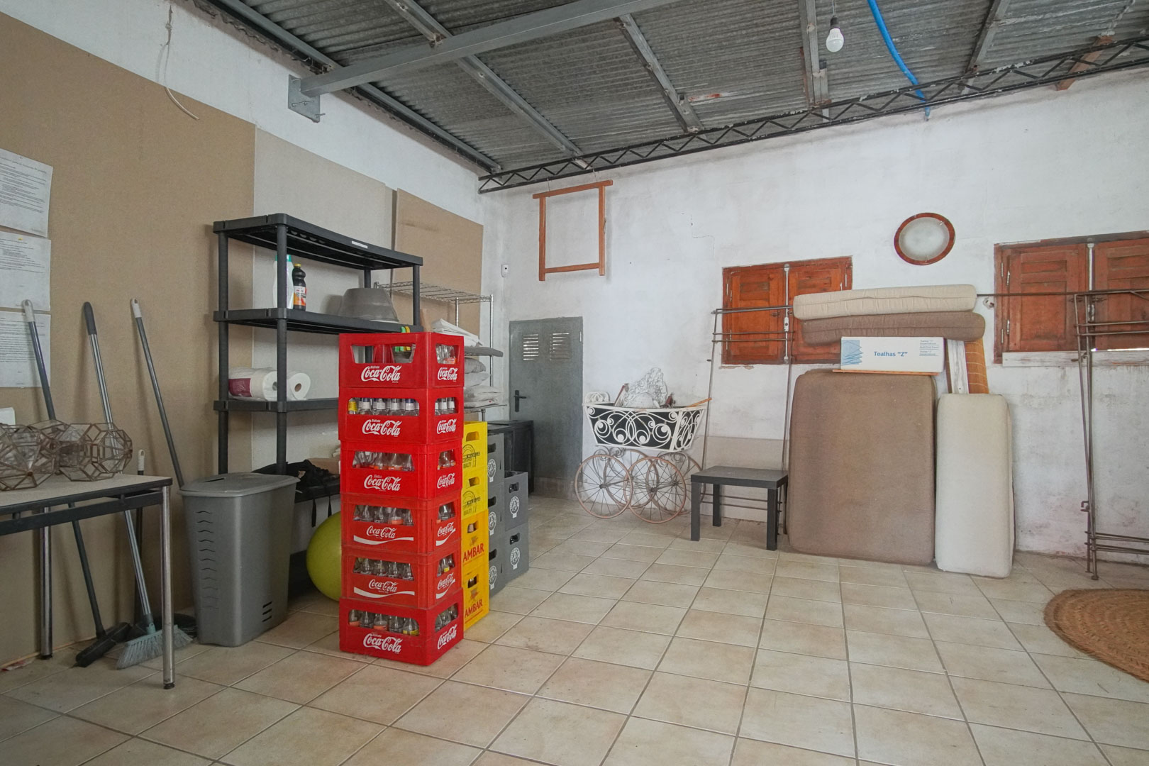 Espacio interior con estanterías metálicas, cajas de refrescos apiladas y objetos diversos sobre suelo de baldosas.