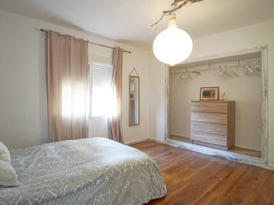 Dormitorio luminoso con cama doble, cortinas rosas y vestidor abierto con cómoda de madera clara.