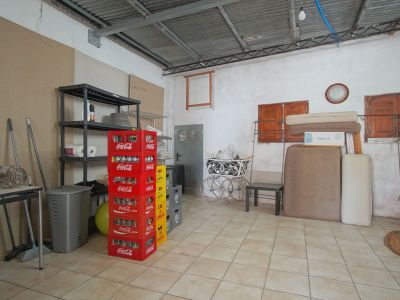 Espacio interior con estanterías metálicas, cajas de refrescos apiladas y objetos diversos sobre suelo de baldosas.