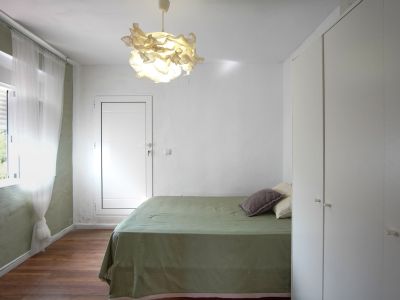 Habitación luminosa con cama cubierta de lino verde, lámpara de diseño y armario empotrado blanco.