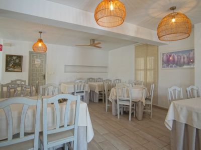 Salón de restaurante con mesas vestidas, sillas de madera clara y lámparas colgantes de mimbre.