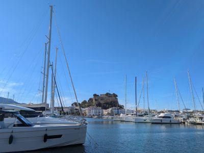 Vista del puerto deportivo de Denia con el castillo histórico en la distancia bajo un cielo azul.