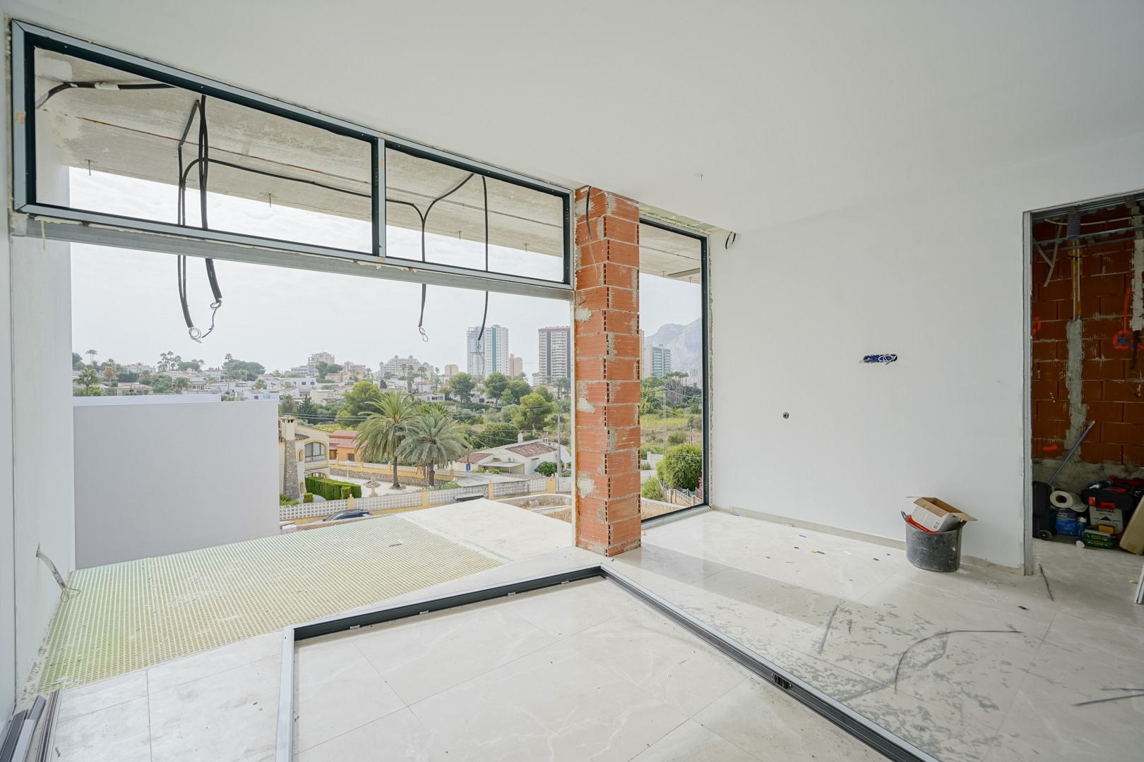Interior en fase de construcción con amplios ventanales de suelo a techo que enmarcan las vistas al Peñón de Ifach y al entorno urbano de Calpe.