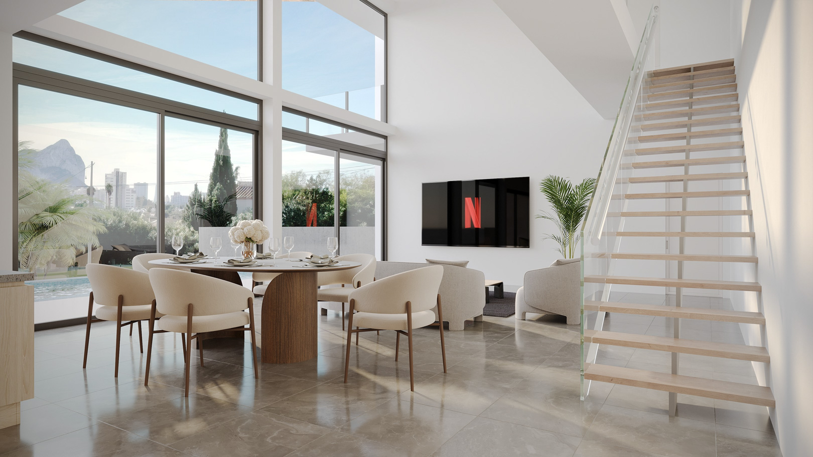 Salón-comedor de doble altura con ventanales panorámicos, vistas al Peñón de Ifach y una escalera de diseño con peldaños de madera y barandilla de cristal.
