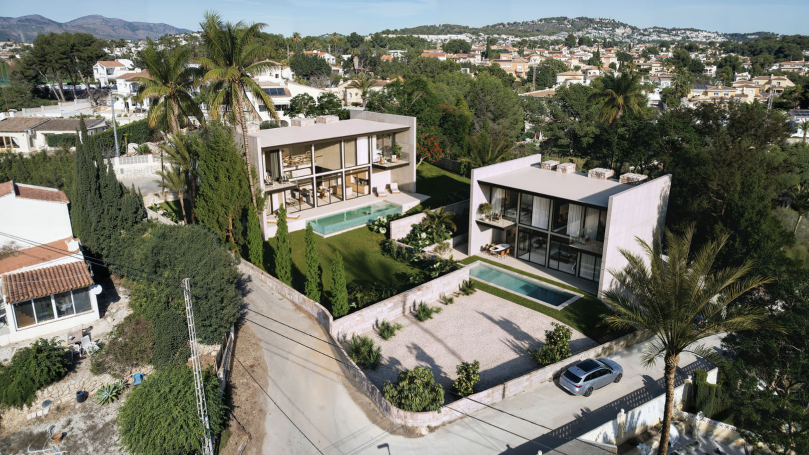 Vista aérea de dos villas contemporáneas con fachadas de vidrio, piscinas rectangulares y jardines con palmeras en la urbanización La Merced de Calpe.