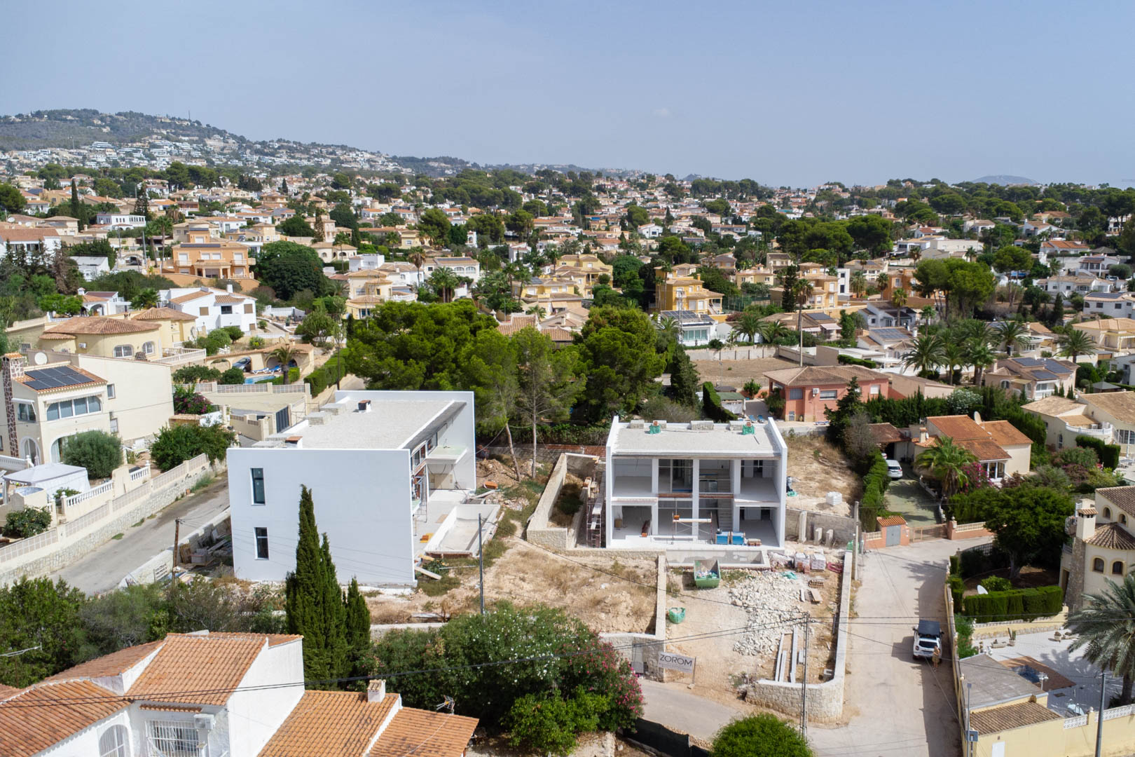 Vista aérea de la villa en construcción en Partida La Merced, Calpe, mostrando la estructura moderna de dos niveles y su ubicación en una zona residencial consolidada.