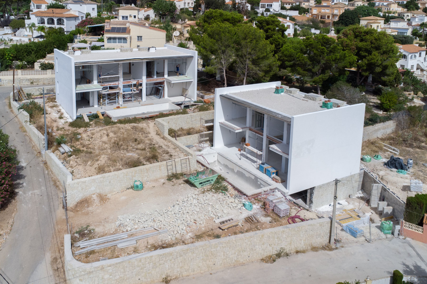 Vista aérea del estado de construcción de las villas modernas, mostrando la estructura de hormigón blanco, muros de piedra perimetrales y las parcelas en fase de obra.