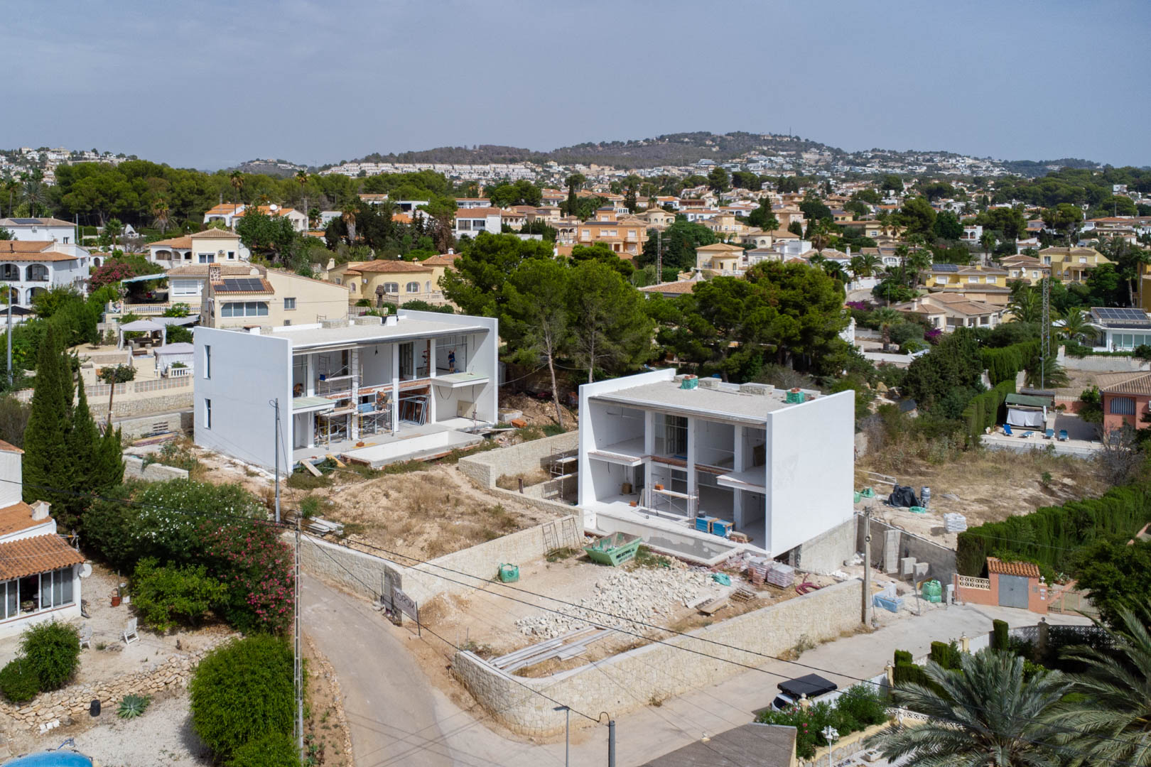 Vista aérea de dos villas modernas en fase de construcción en Calpe, con estructuras blancas de dos niveles y muros perimetrales de piedra natural.