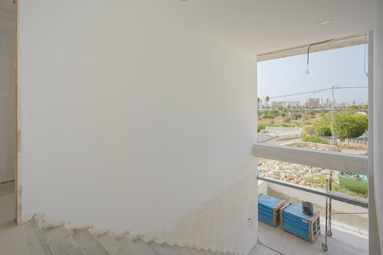 Vista desde la escalera en construcción hacia el exterior, mostrando los amplios ventanales y el entorno urbano de Calpe durante la fase de obra.