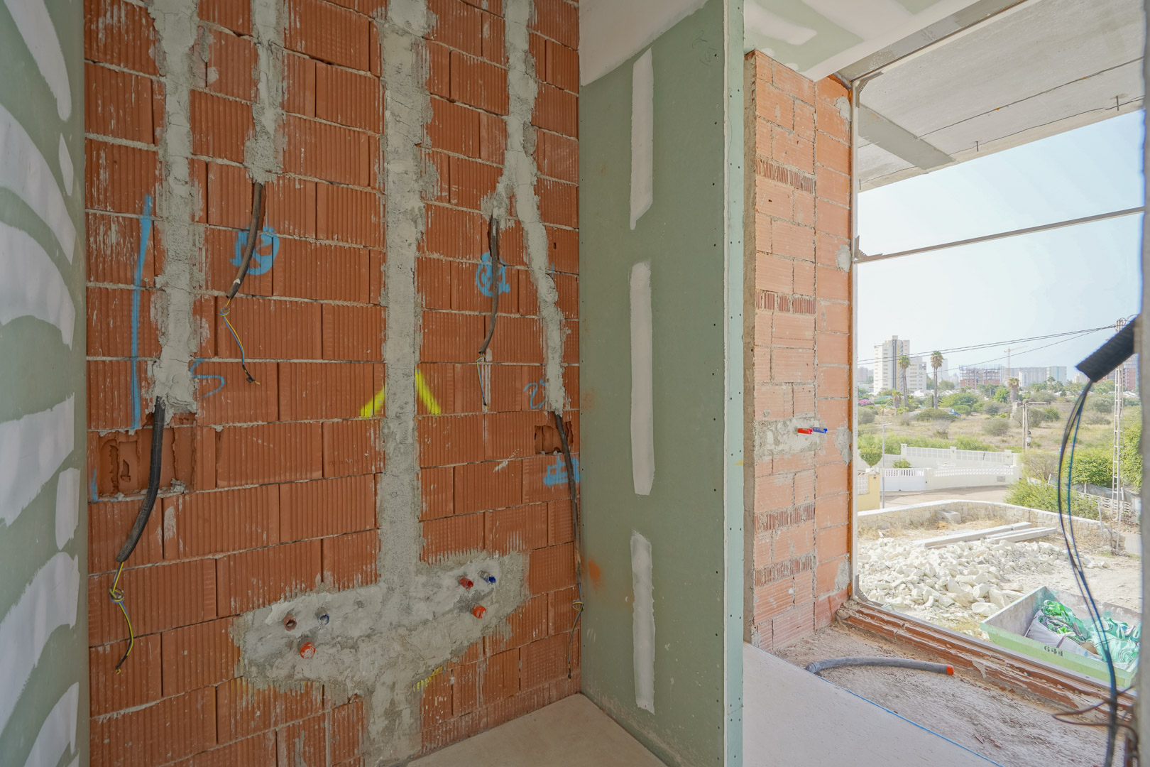 Vista interior de la fase de construcción con tabiquería de ladrillo, instalaciones eléctricas y tomas de agua frente a un gran ventanal con vistas despejadas.