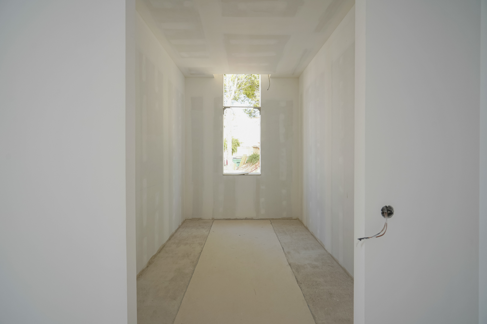 Vista interior de la zona de vestidor en construcción, destacando el ventanal vertical que aporta luz natural y las paredes de placa de yeso laminado.