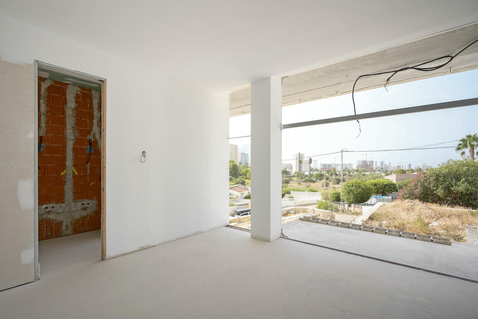 Vista interior de un dormitorio en obra con amplios ventanales y vistas despejadas hacia el perfil urbano de Calpe y el Peñón de Ifach.