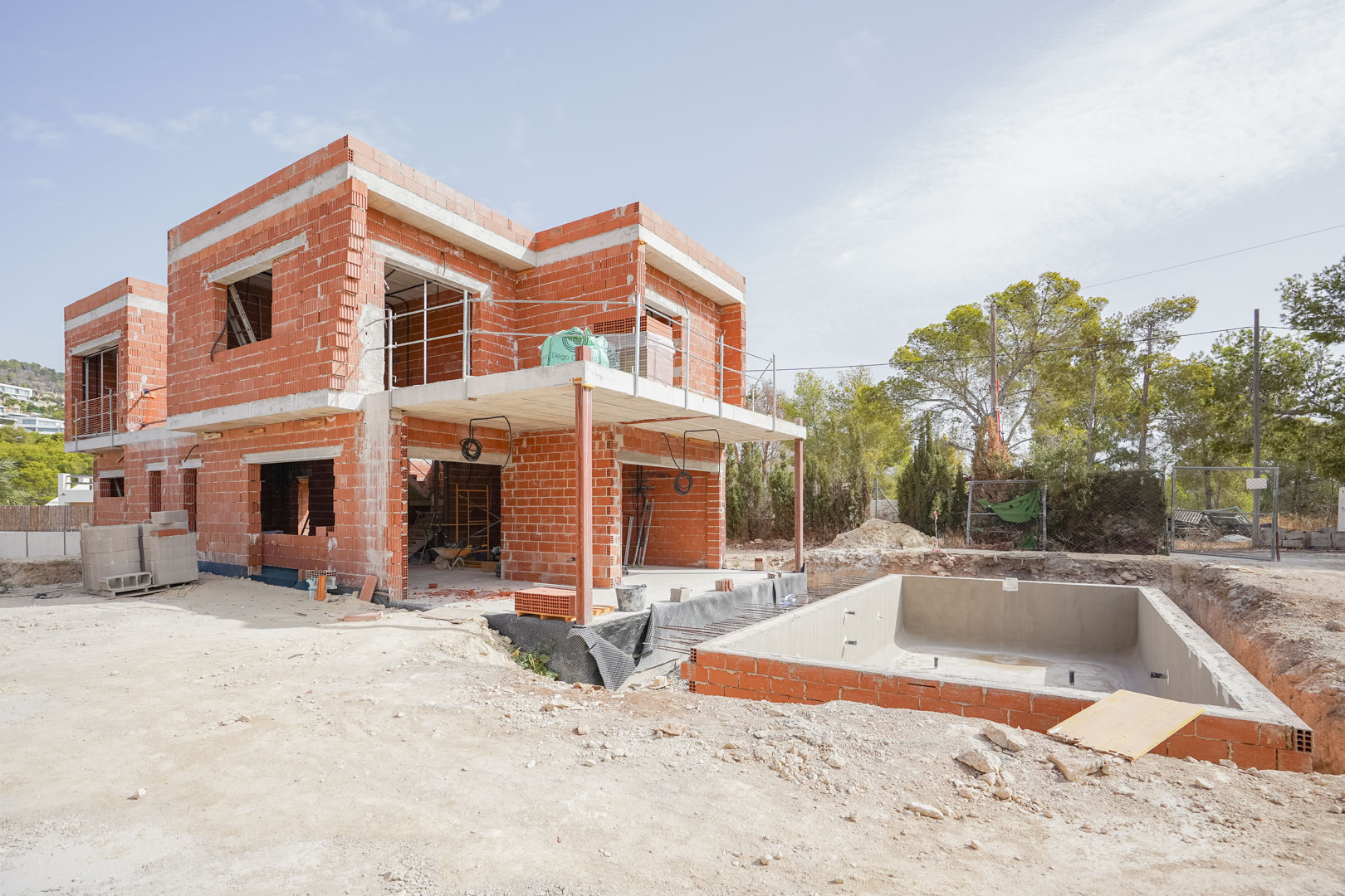Estado actual de la construcción mostrando la estructura de ladrillo cerámico, forjados de hormigón y el vaso de la piscina ya definido en la parcela.