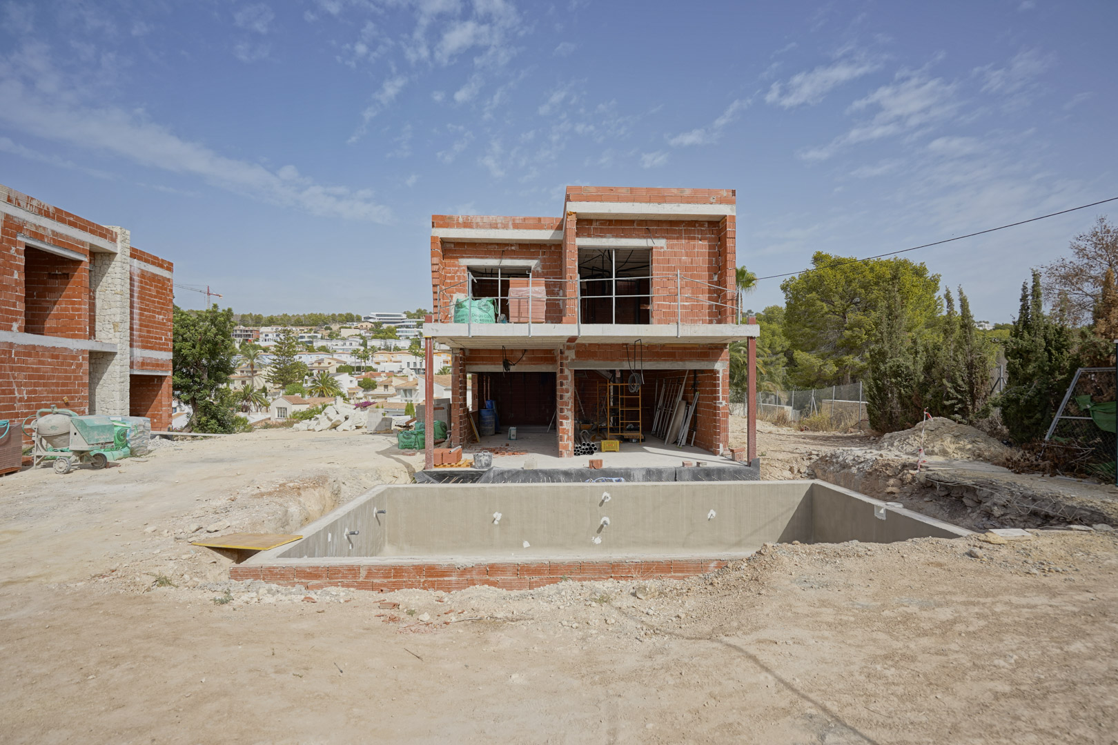 Villa en fase de obra con estructura de ladrillo visto y forjados de hormigón. Se aprecia el vaso de la piscina y la distribución de dos plantas orientada al sur.