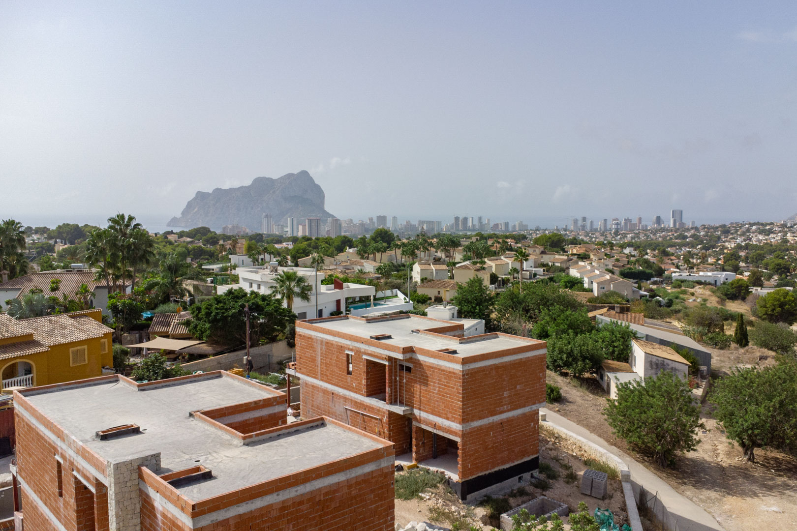 Vista aérea de la fase de construcción de las villas, destacando la estructura de ladrillo y las vistas panorámicas al Peñón de Ifach y al skyline de Calpe.