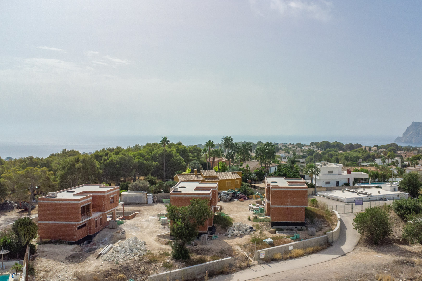 Vista aérea del estado de construcción de las tres villas de lujo, mostrando las estructuras de ladrillo y las vistas panorámicas al mar y al Peñón de Ifach.