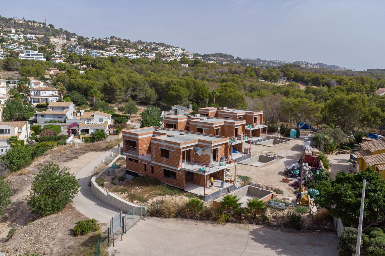 Vista aérea del estado de construcción de las tres villas, destacando las estructuras de ladrillo y los fosos de las piscinas privadas en una zona residencial rodeada de pinos.