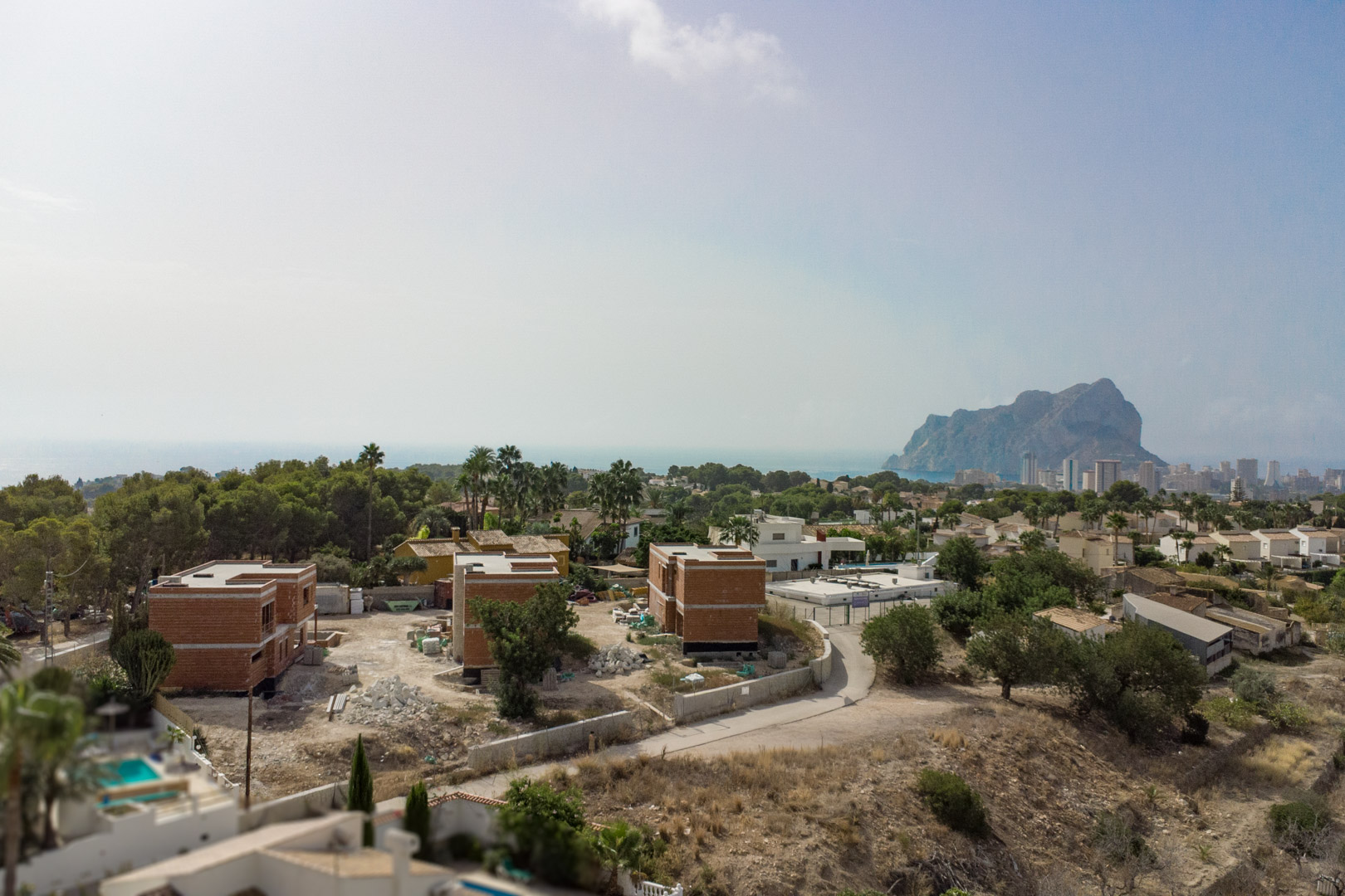 Vista aérea del estado de construcción de las tres villas en Partida Gran Sol, con el Peñón de Ifach y el skyline de Calpe al fondo sobre el mar Mediterráneo.